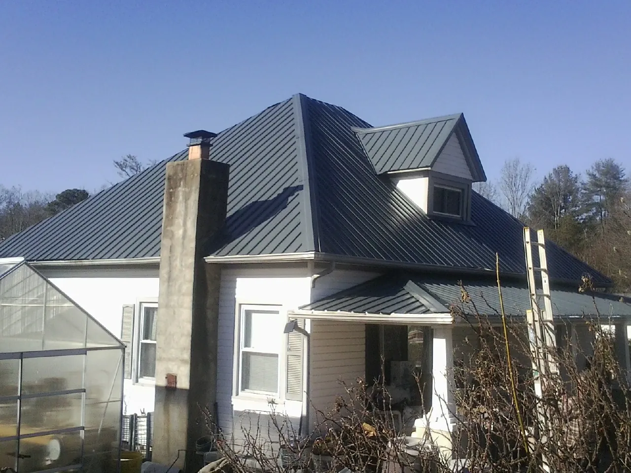 Dark blue standing seam metal roof on a white farmhouse with dormer — Slate & Tile Roof Repair by Roofing Brothers in Cofield