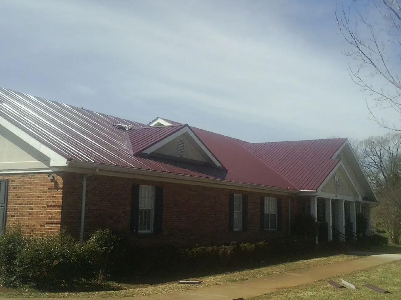 Red metal roof with gabled entries on a long brick building, from a Hail Damage Roof Repair job in Cofield