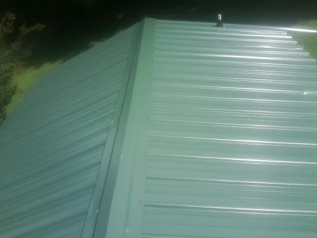 New green metal panels meeting at the ridge of a roof — Flat Roof Repair work by our crew in Cofield