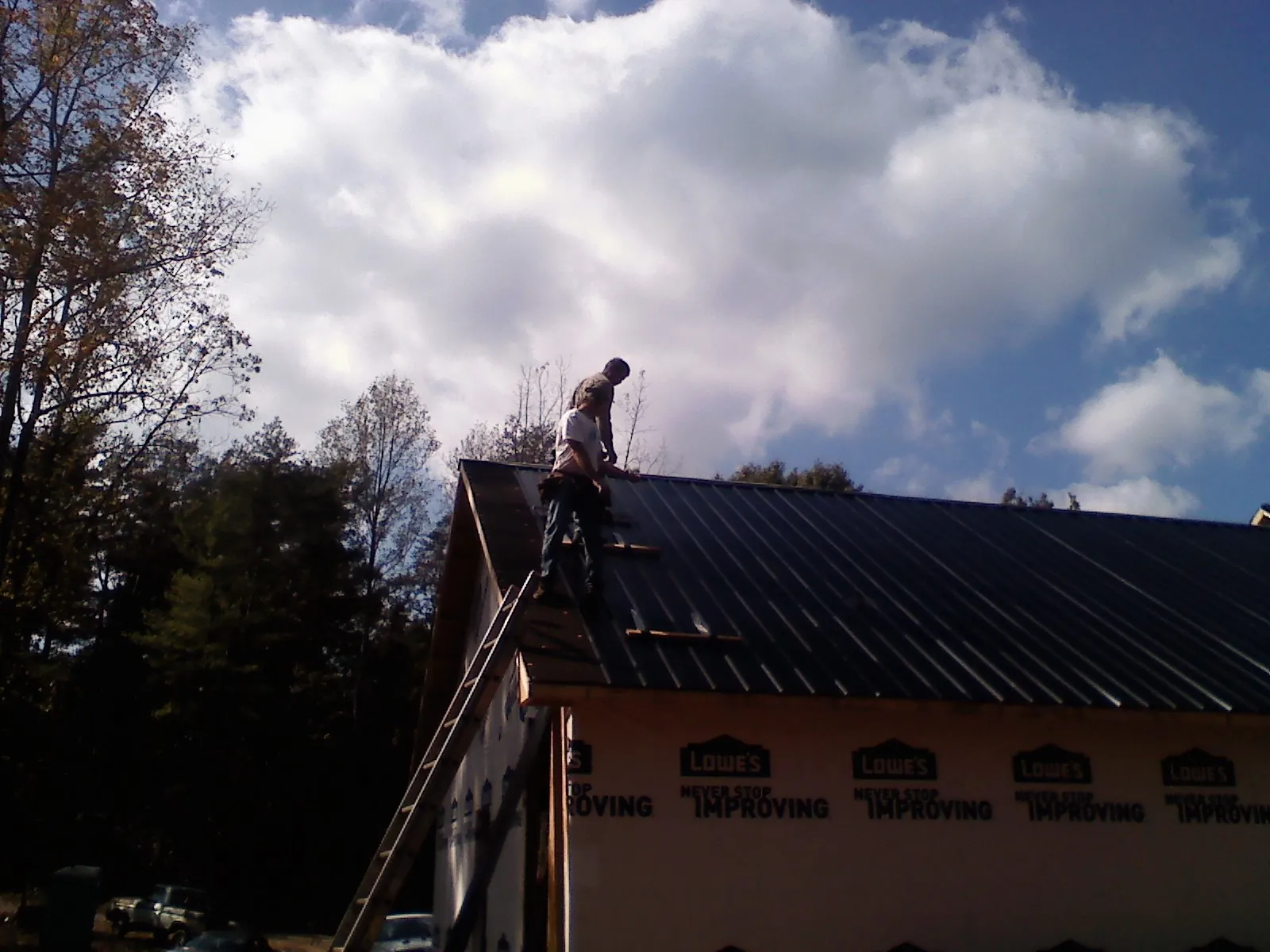 Roofer fastening dark metal panels high against a cloudy sky, from a Roof Inspection job in Cofield