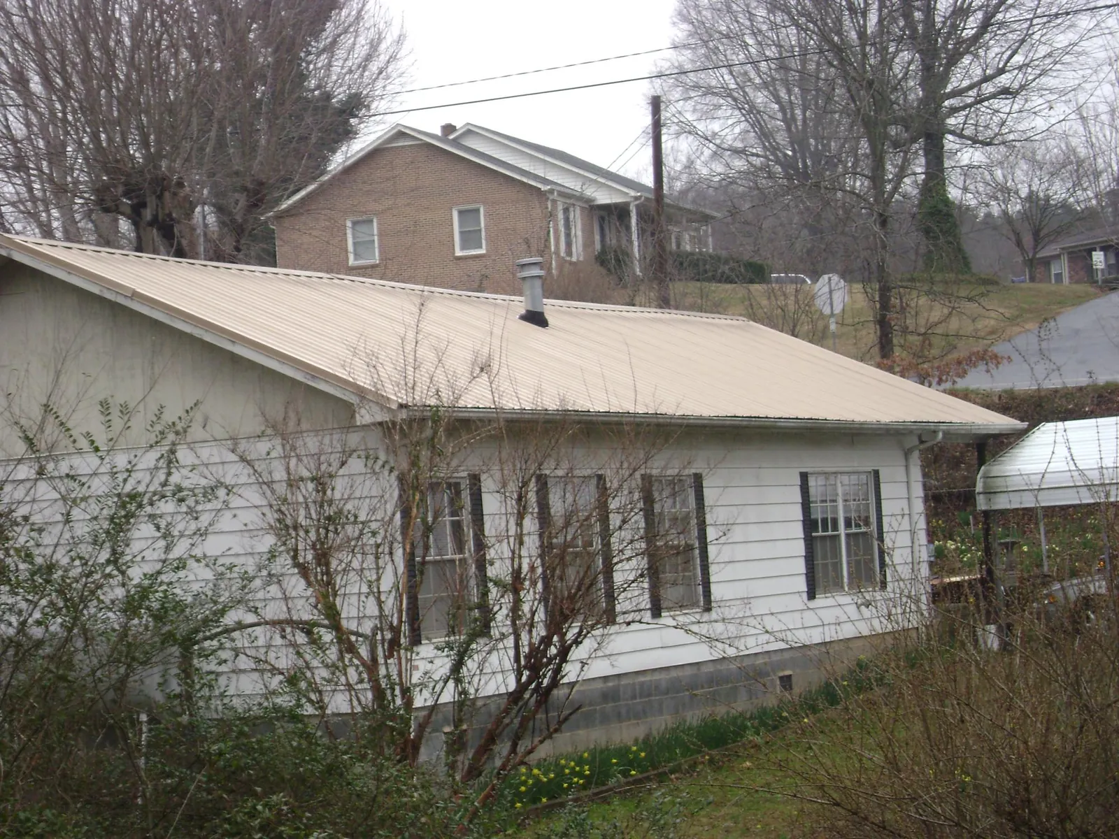 Tan metal roof on a white sided house set into a hillside — Commercial Roofing by Roofing Brothers in Cofield